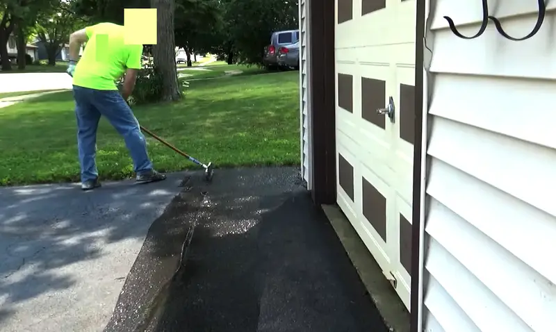 Ouvrier utilisant une raclette en caoutchouc pour appliquer et lisser le scellant sur une allée d'asphalte