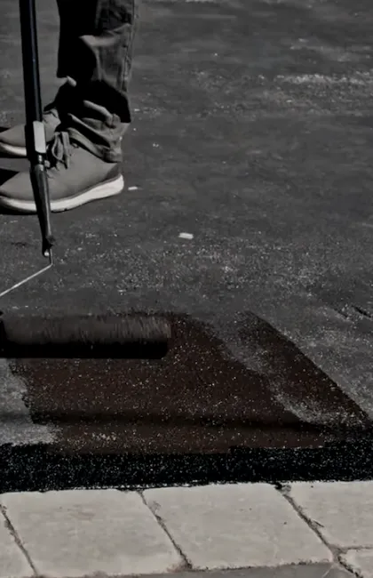 Close-up of a worker using a driveway sealer roller for asphalt driveway maintenance. The professional application of asphalt driveway sealant ensures a long-lasting, protected finish.